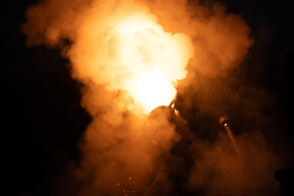 Cannon firing with a bright burst of flame and thick smoke against a dark background