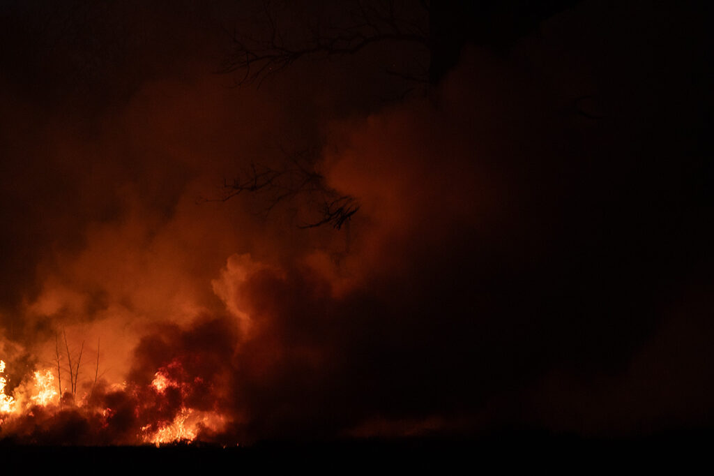 Large fire burning at night with heavy smoke and glowing flames against a dark sky