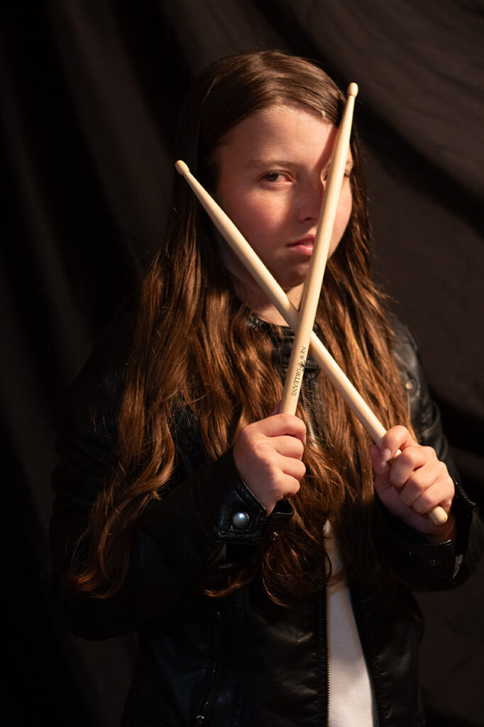 Portrait of a young woman holding drumsticks with dramatic lighting against a dark background