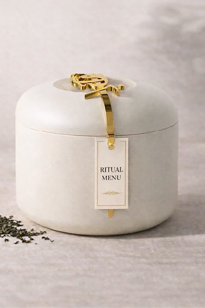 Yūgen Tea Atelier ritual to-go packaging featuring a minimal white container with gold detailing and hanging tag.